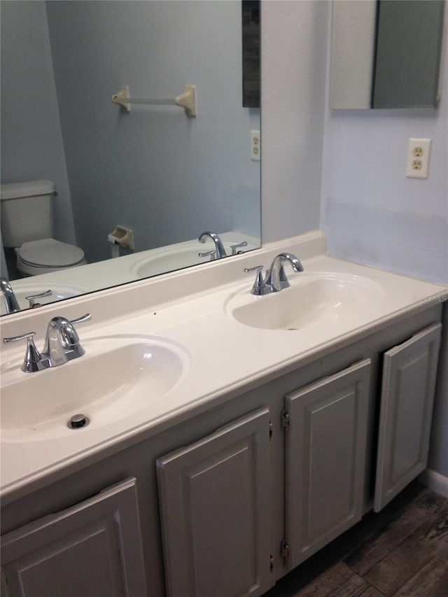 bathroom with toilet, double vanity, a sink, and wood finished floors