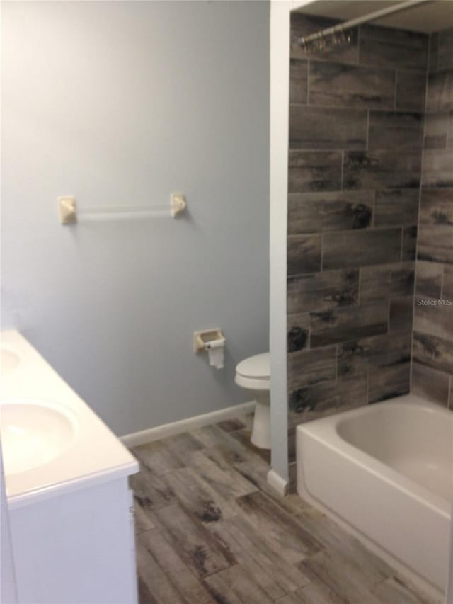 bathroom featuring shower / tub combination, toilet, wood finished floors, a sink, and double vanity