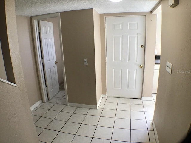 hallway with a textured ceiling, light tile patterned floors, and baseboards