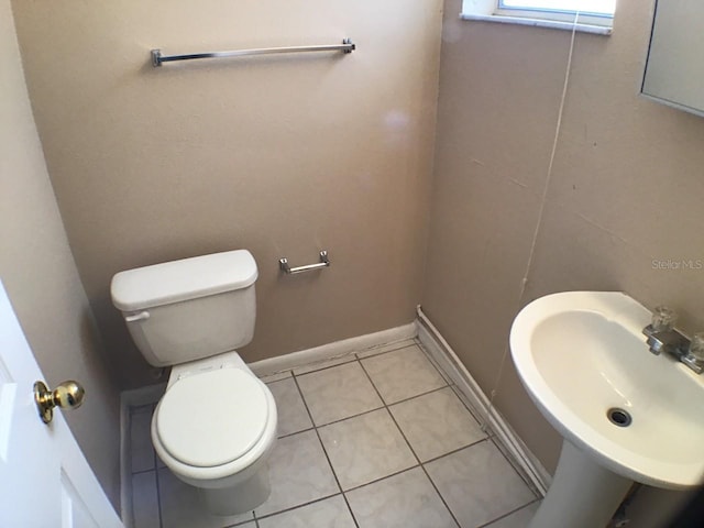 half bathroom featuring toilet, baseboards, a sink, and tile patterned floors