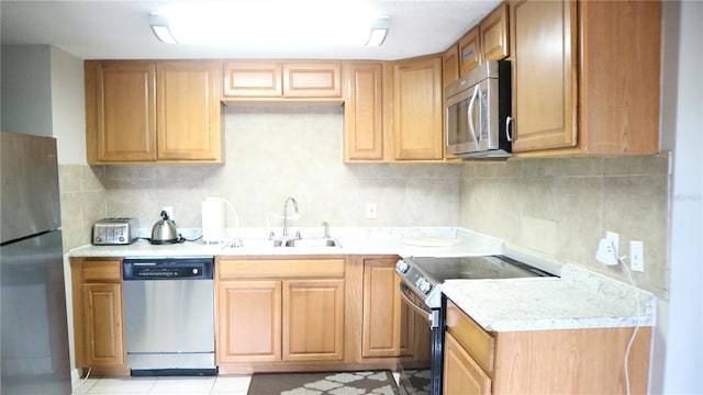 kitchen with appliances with stainless steel finishes, sink, light stone counters, and decorative backsplash