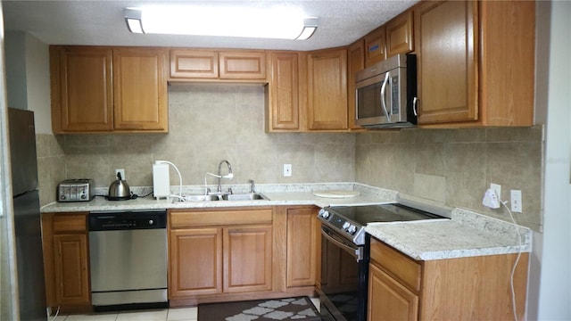 kitchen with appliances with stainless steel finishes, sink, light stone countertops, and decorative backsplash