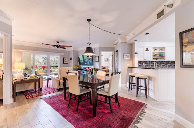 dining space with light wood-style floors, visible vents, crown molding, and baseboards