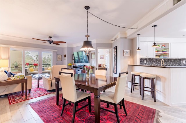 dining room with ceiling fan with notable chandelier, light wood finished floors, visible vents, and crown molding