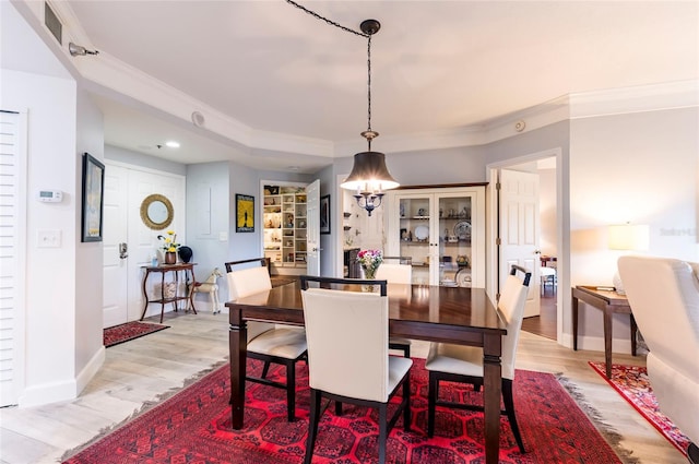 dining room with light wood-type flooring, baseboards, visible vents, and ornamental molding