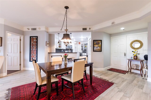 dining area with light wood-style flooring, ornamental molding, and baseboards