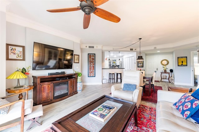 living room with light wood-style floors, crown molding, baseboards, and a ceiling fan