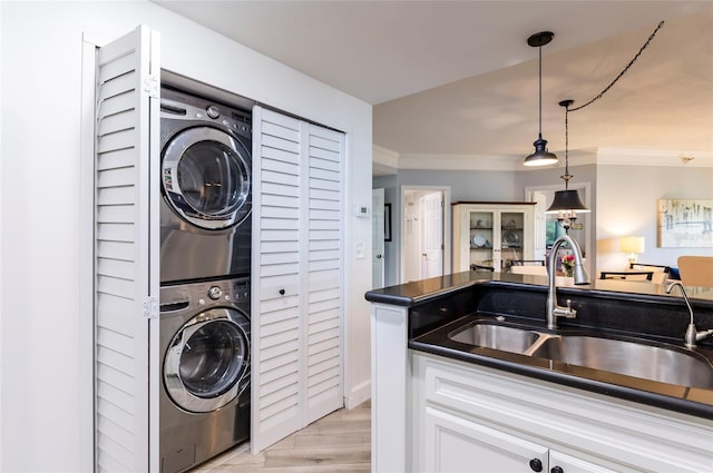 clothes washing area featuring laundry area, a sink, stacked washer / drying machine, light wood-type flooring, and crown molding