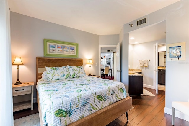 bedroom with visible vents, connected bathroom, baseboards, and wood finished floors