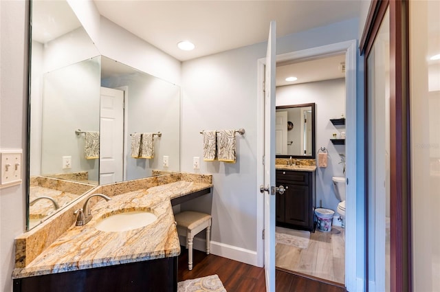 full bath with baseboards, toilet, two vanities, wood finished floors, and a sink