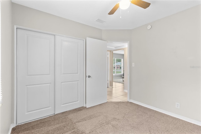 unfurnished bedroom featuring light tile patterned floors, baseboards, a ceiling fan, light colored carpet, and a closet