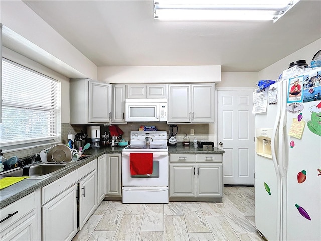 kitchen featuring white appliances, dark countertops, and a sink