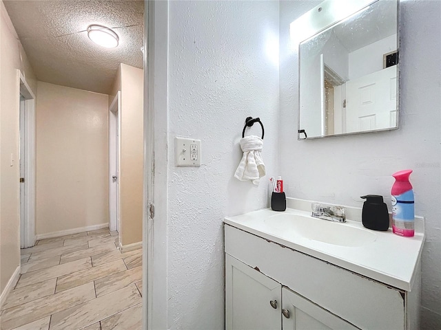 bathroom featuring a textured ceiling, a textured wall, wood finish floors, vanity, and baseboards