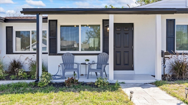 view of exterior entry featuring covered porch and stucco siding