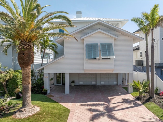 8505 Blind Pass Dr, Treasure Island, FL 33706 - view of front facade featuring an attached garage, fence, central air condition unit, decorative driveway, and a chimney