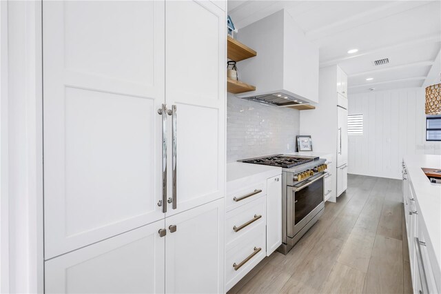 8505 Blind Pass Dr, Treasure Island, FL 33706 - kitchen featuring high end appliances, wall chimney exhaust hood, white cabinets, light countertops, and light wood-type flooring