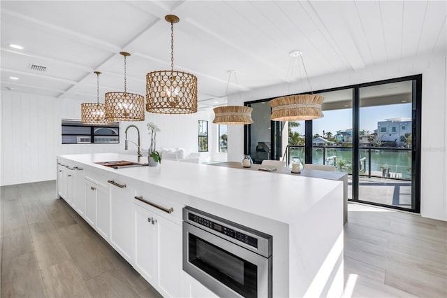 8505 Blind Pass Dr, Treasure Island, FL 33706 - kitchen with a sink, stainless steel microwave, light wood-style floors, white cabinetry, and decorative light fixtures
