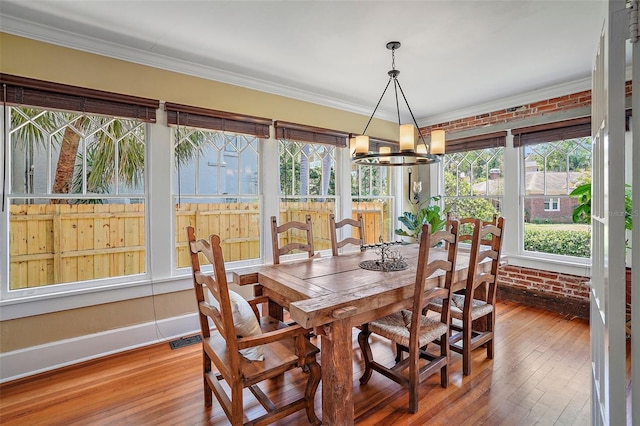 dining space with brick wall, crown molding, and wood finished floors