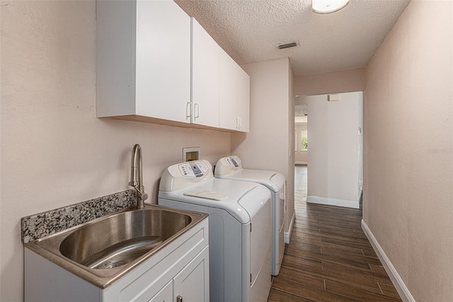 clothes washing area featuring dark wood-type flooring, a textured ceiling, washer and clothes dryer, sink, and cabinets