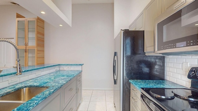 kitchen with light tile patterned floors, decorative backsplash, appliances with stainless steel finishes, a sink, and dark stone countertops