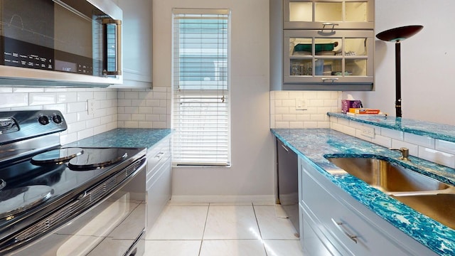 kitchen featuring baseboards, glass insert cabinets, gray cabinets, black appliances, and a sink