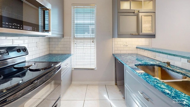 kitchen featuring gray cabinetry, a sink, baseboards, black appliances, and glass insert cabinets