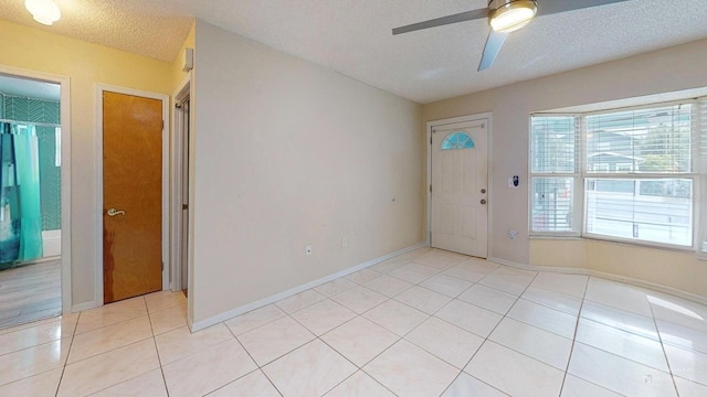 empty room featuring ceiling fan, baseboards, a textured ceiling, and light tile patterned flooring