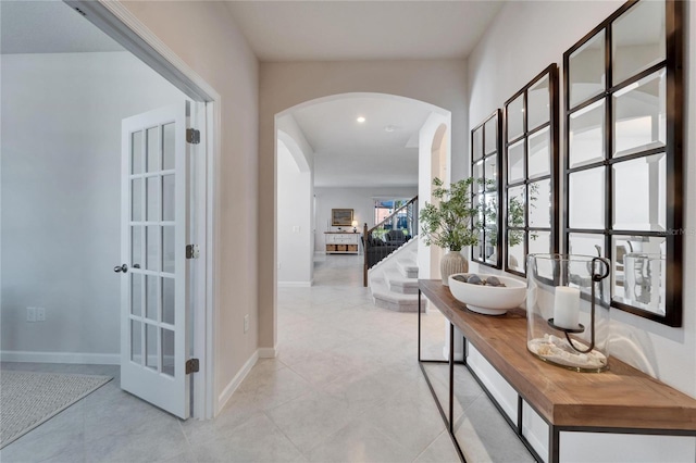 hallway featuring arched walkways, stairway, baseboards, and recessed lighting