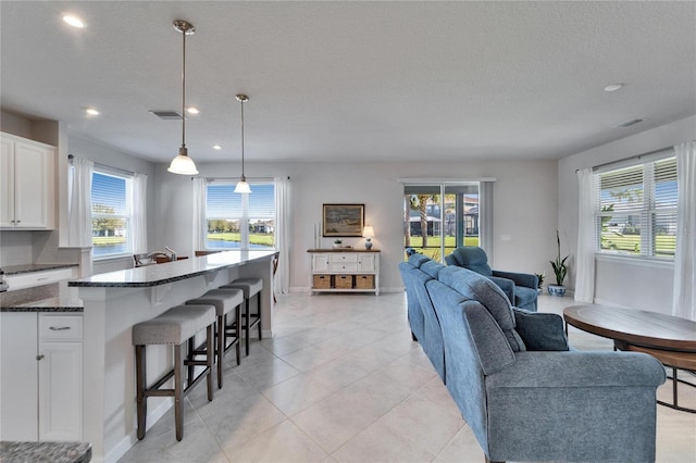 living area featuring a textured ceiling, light tile patterned floors, recessed lighting, visible vents, and baseboards