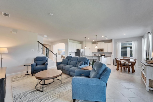 living room featuring arched walkways, visible vents, stairway, light tile patterned flooring, and baseboards