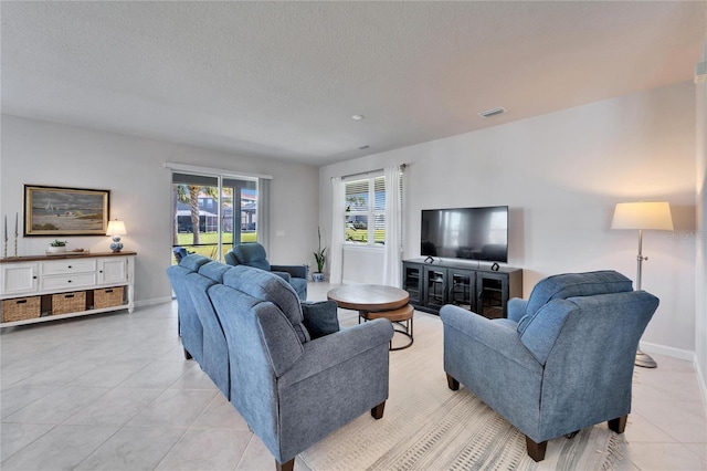 living area with light tile patterned floors, baseboards, visible vents, and a textured ceiling