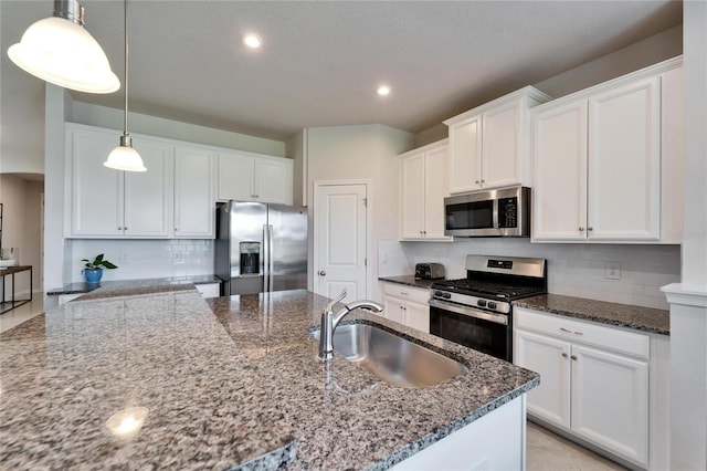 kitchen featuring appliances with stainless steel finishes, dark stone countertops, decorative light fixtures, white cabinetry, and a sink