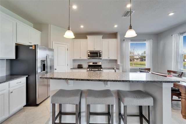 kitchen with white cabinets, appliances with stainless steel finishes, visible vents, and a center island