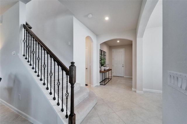 interior space with arched walkways, light tile patterned floors, recessed lighting, stairway, and baseboards