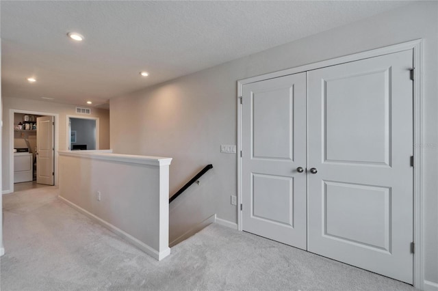 hallway with washer / dryer, visible vents, light colored carpet, an upstairs landing, and recessed lighting