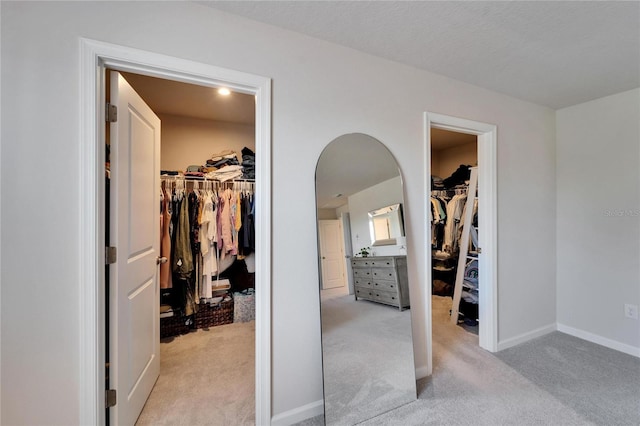 interior space featuring baseboards, a closet, a walk in closet, and light colored carpet