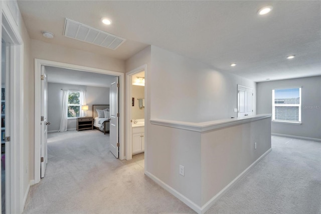 hall with recessed lighting, light carpet, a sink, visible vents, and baseboards