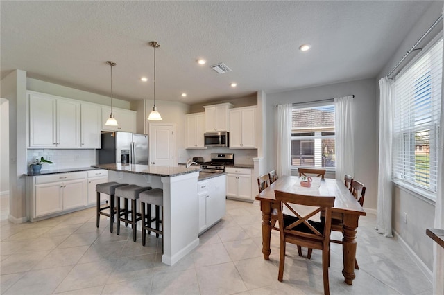 kitchen featuring a center island with sink, visible vents, dark stone counters, appliances with stainless steel finishes, and white cabinetry