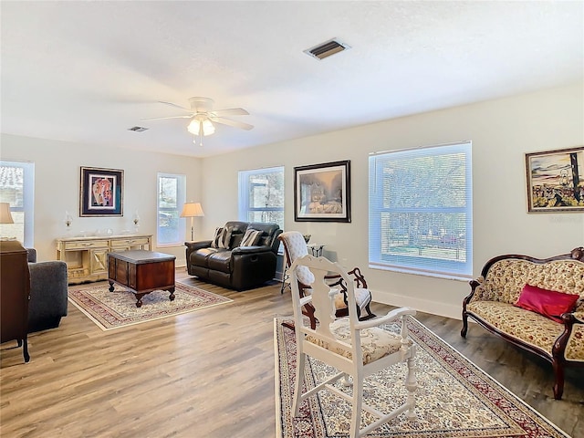 living area with ceiling fan, light wood finished floors, visible vents, and baseboards