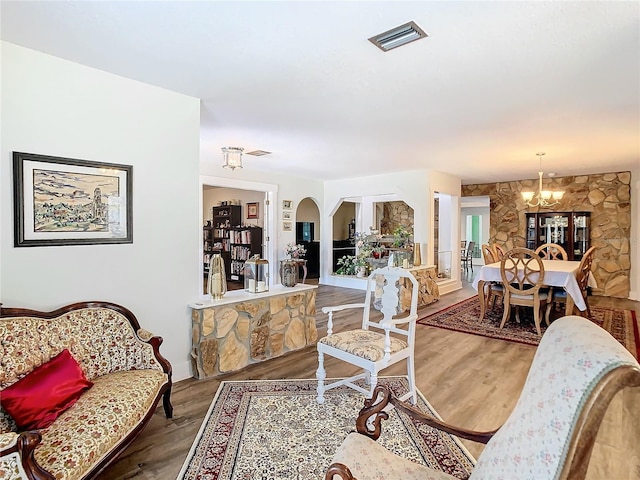 living area with a chandelier, arched walkways, visible vents, and wood finished floors