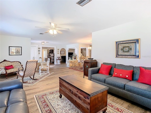 living area with light wood-type flooring, visible vents, arched walkways, and ceiling fan with notable chandelier