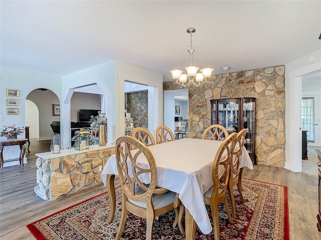 dining area featuring arched walkways, an inviting chandelier, and wood finished floors