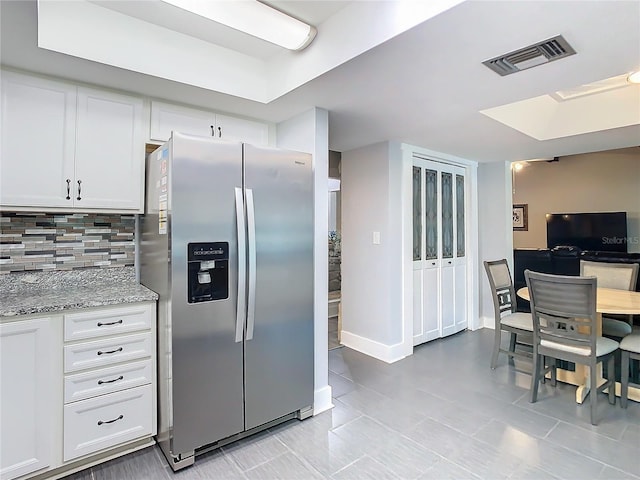 kitchen with light stone counters, visible vents, white cabinets, stainless steel refrigerator with ice dispenser, and backsplash