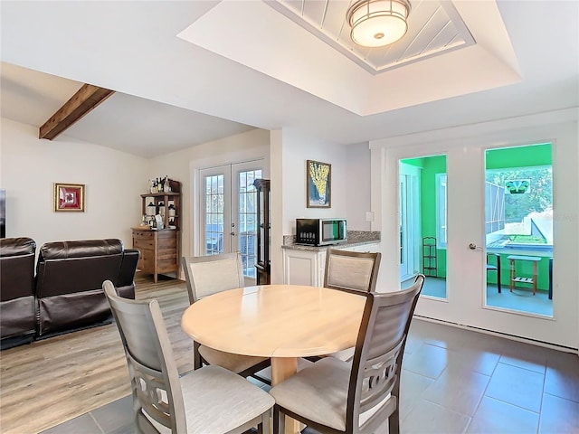 dining area featuring light tile patterned floors, a tray ceiling, a wealth of natural light, and french doors