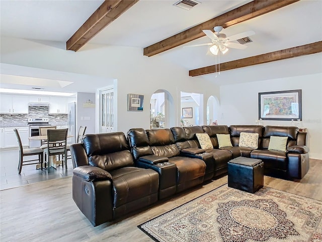 living area featuring light wood-type flooring, visible vents, arched walkways, and beamed ceiling