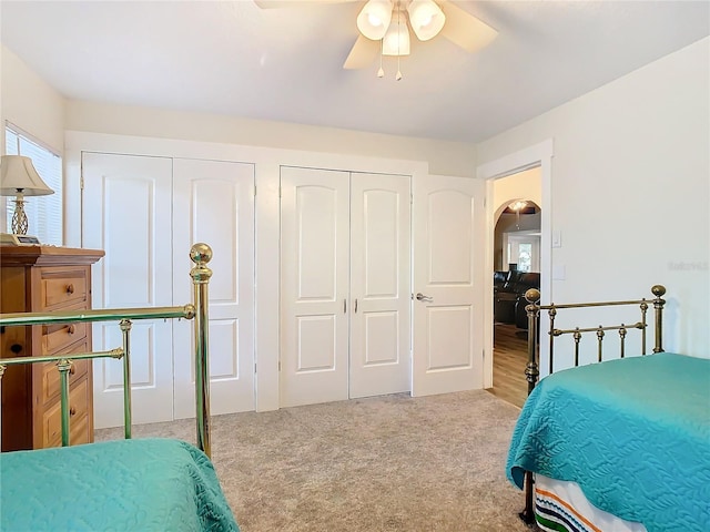 bedroom featuring arched walkways, multiple closets, a ceiling fan, and light colored carpet