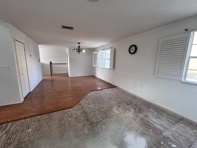 unfurnished room with a chandelier, wood finished floors, visible vents, and baseboards