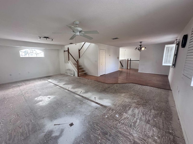 basement featuring stairs, visible vents, a textured ceiling, and ceiling fan with notable chandelier