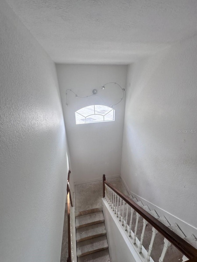 staircase featuring a textured wall and a textured ceiling