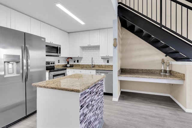 kitchen featuring stainless steel appliances, white cabinets, a kitchen island, a sink, and light stone countertops